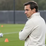 Een staflid kijkt vanaf de zijlijn naar een trainingsopstelling op een voetbalveld.