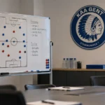 Leeg analyse­lokaal van KAA Gent met een tactiekbord en een clubembleem aan de wand.