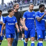 Spelers en een staflid van KAA Gent staan naast het veld na een wedstrijd.
