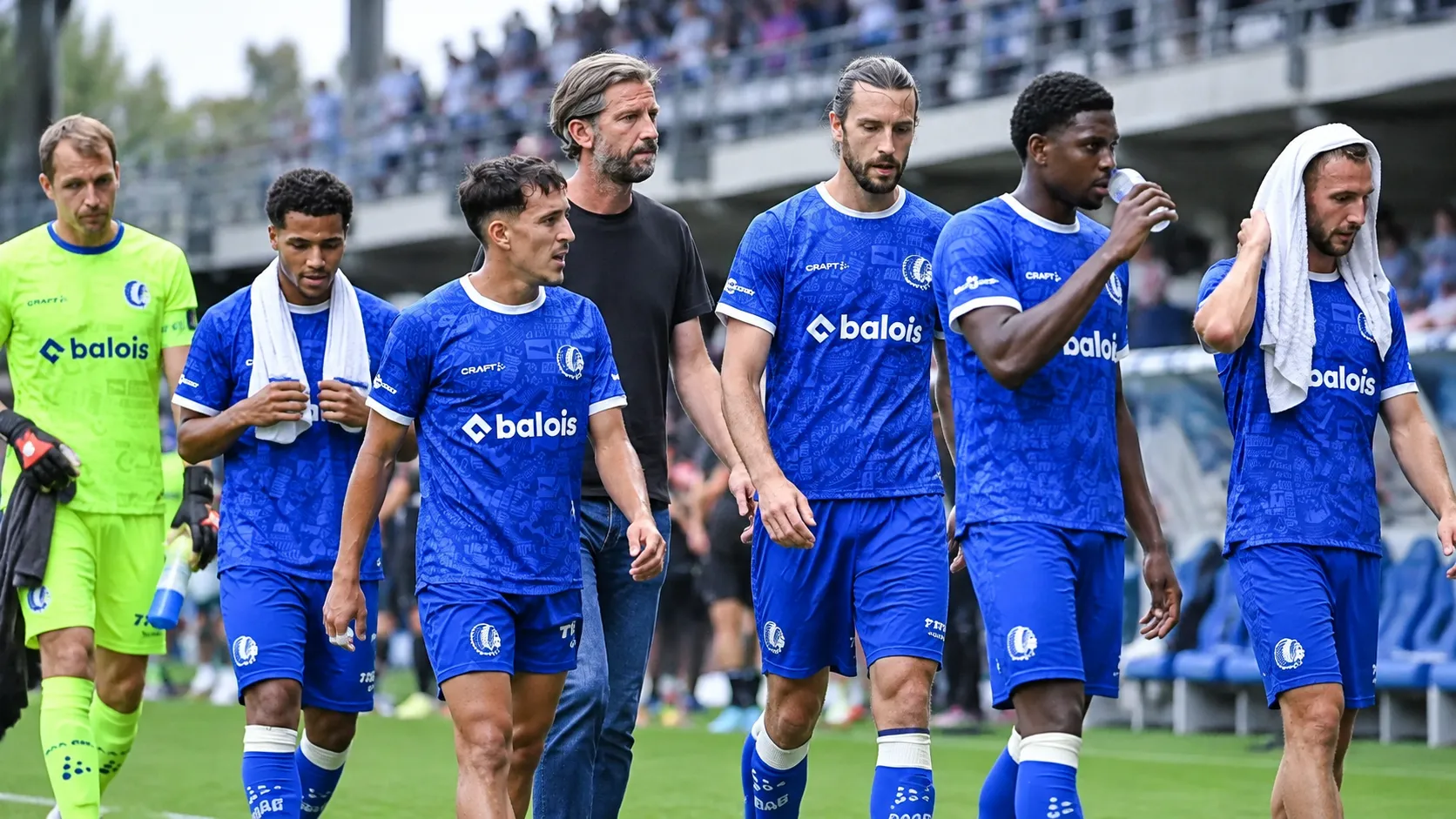Spelers en een staflid van KAA Gent staan naast het veld na een wedstrijd.