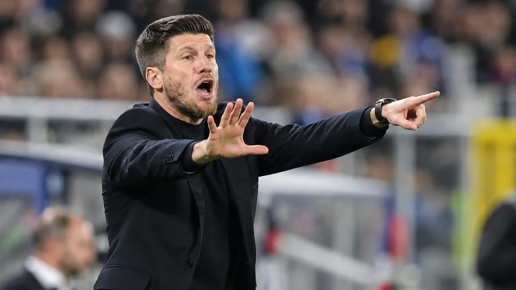 Sébastien Pocognoli in donkere coachkleding terwijl hij langs de zijlijn aanwijzingen geeft.