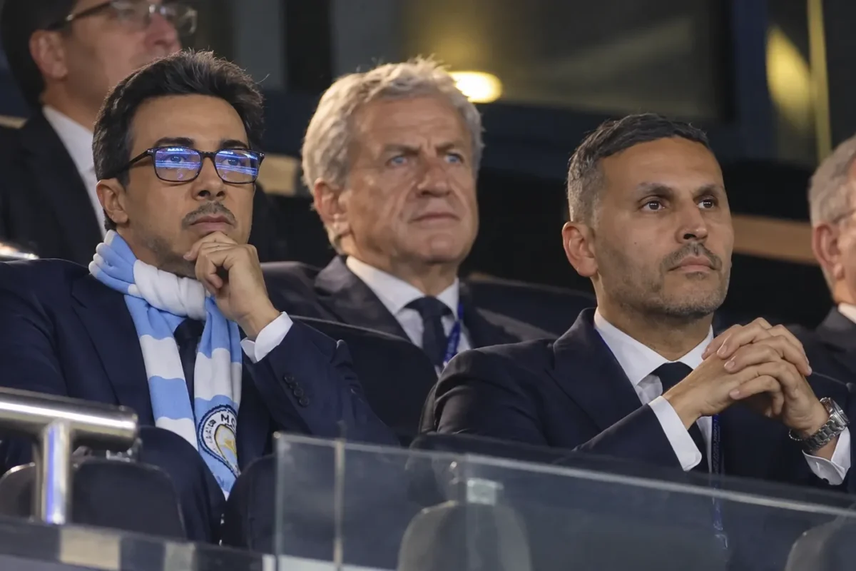 Niet-spelende clubvertegenwoordigers van Manchester City in de tribune van een stadion.