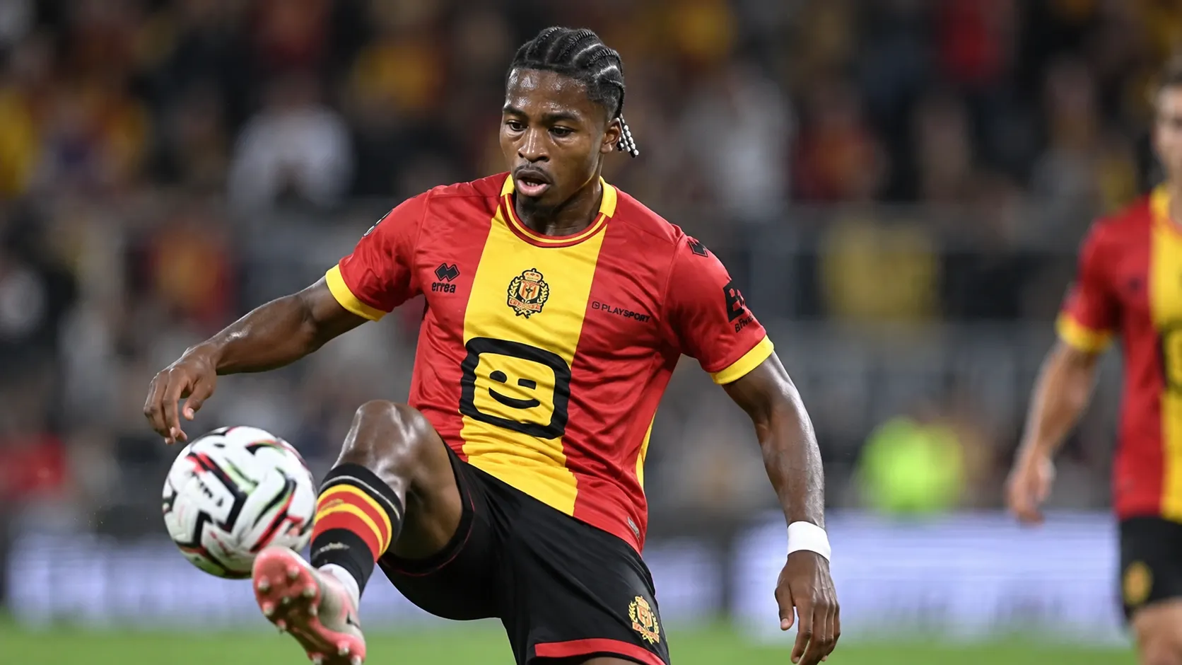 Simion Michez van KV Mechelen controleert de bal in een verlichte voetbalomgeving.