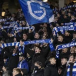 Een groep KRC Genk-supporters met blauwe sjaals op de tribune.
