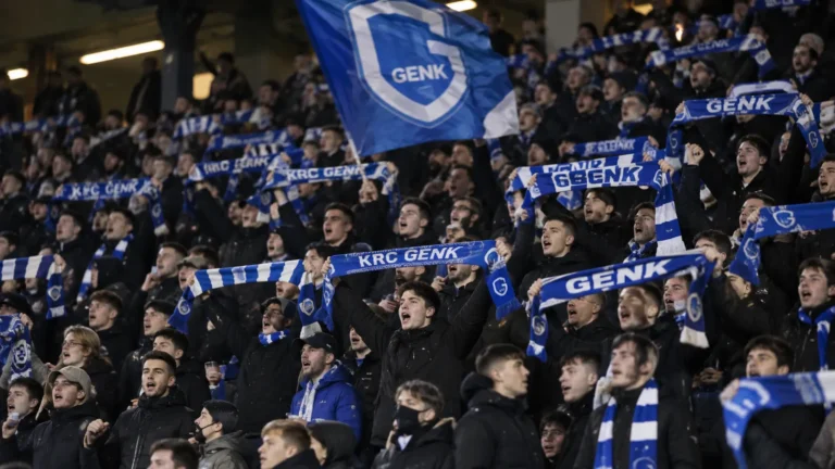 Een groep KRC Genk-supporters met blauwe sjaals op de tribune.