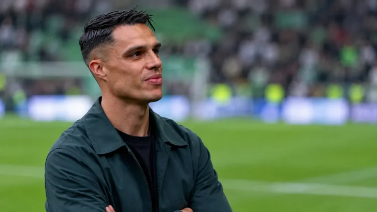Joey Pelupessy in een donkere jas langs de rand van een voetbalveld.