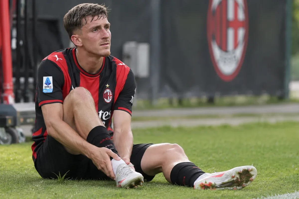 Alexis Saelemaekers van AC Milan staat aan de rand van een trainingsveld met zijn hand bij de enkel.