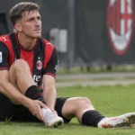 Alexis Saelemaekers van AC Milan staat aan de rand van een trainingsveld met zijn hand bij de enkel.