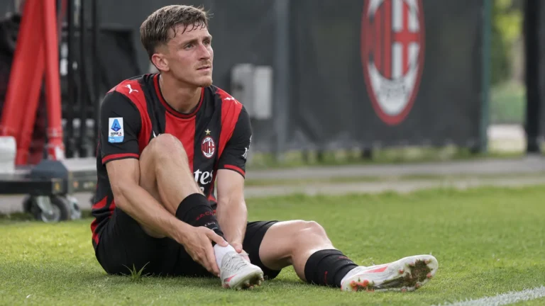 Alexis Saelemaekers van AC Milan staat aan de rand van een trainingsveld met zijn hand bij de enkel.