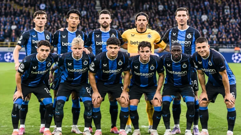 Een groep spelers van Club Brugge in blauw-zwarte tenues poseert in een stadion.