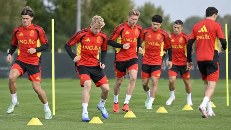 Een groep nationale ploegspelers in rode trainingskleding tijdens een behendigheidsoefening op het trainingsveld.