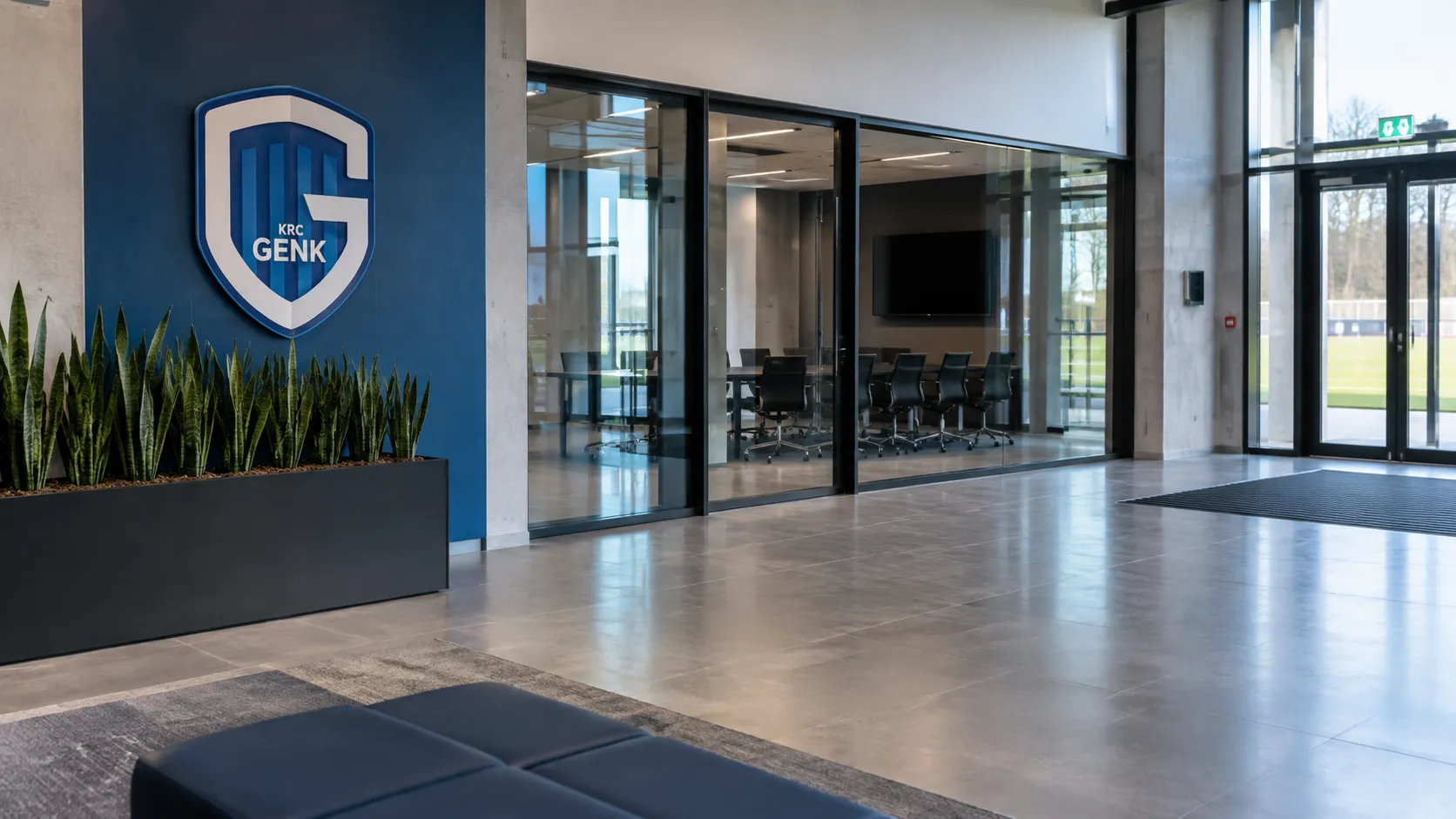 Lege inkomhal van de jeugdacademie van KRC Genk met een clubembleem op een vaste wandplaat.