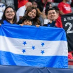 Een groep supporters houdt een blauw-witte Hondurese vlag vast op de tribune.