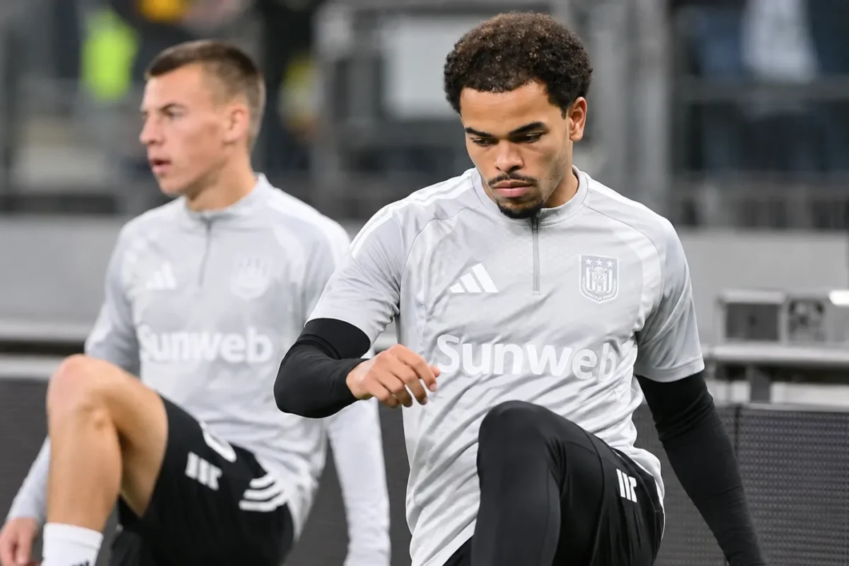 Twee voetballers in grijze opwarmkleding tijdens een moment naast het veld.