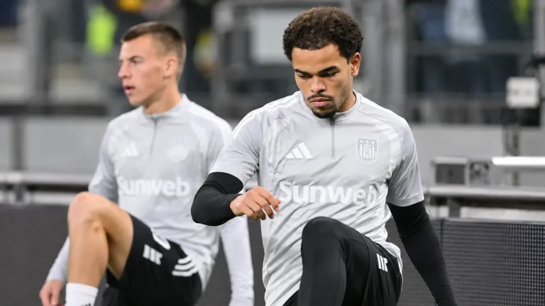 Twee voetballers in grijze opwarmkleding tijdens een moment naast het veld.