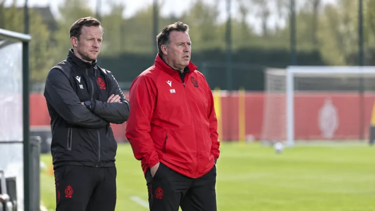 Twee stafleden van Standard volgen een training langs het veld.