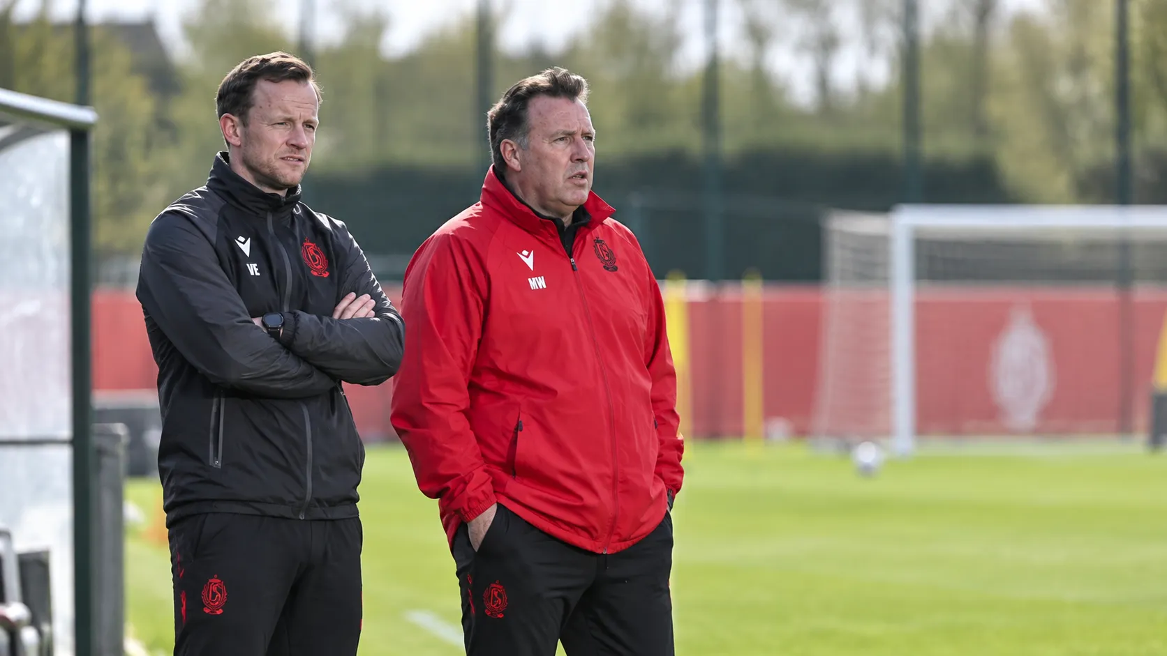 Twee stafleden van Standard volgen een training langs het veld.