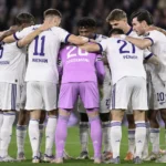 Een groep Anderlecht-spelers vormt een hechte kring op het veld, met een doelman in paars tenue.