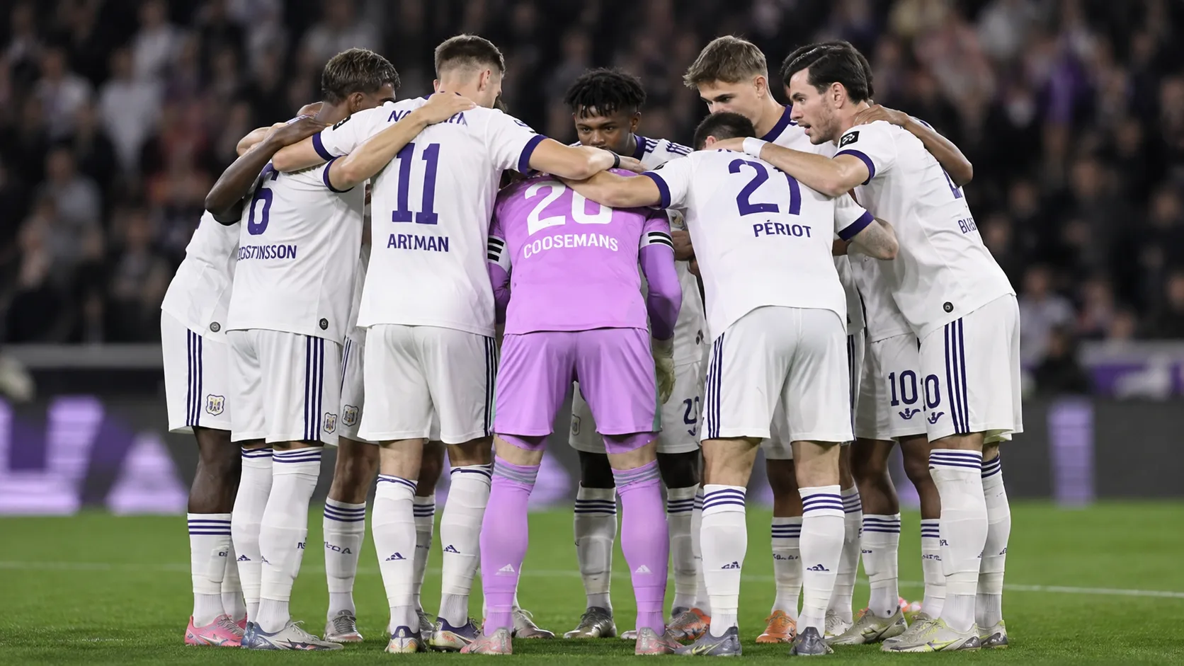 Een groep Anderlecht-spelers vormt een hechte kring op het veld, met een doelman in paars tenue.