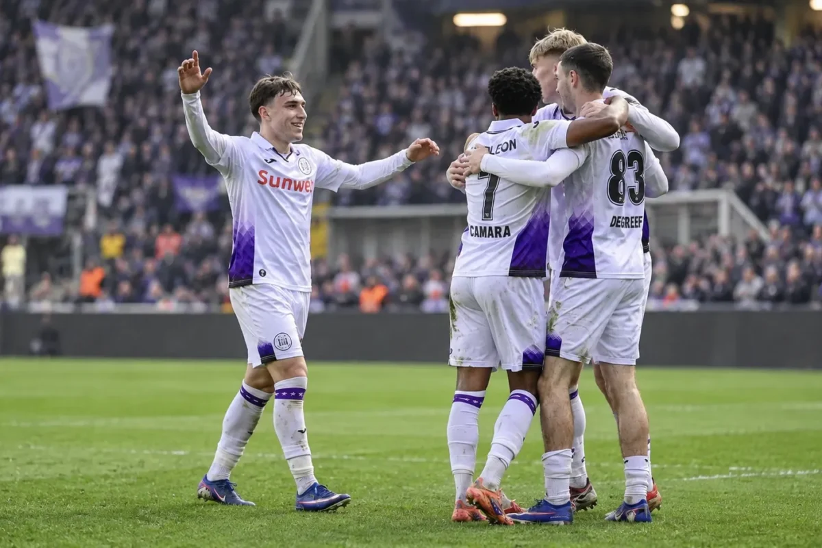 Een groep Anderlecht-spelers viert samen op het veld in wit-paars tenue.