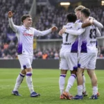 Een groep Anderlecht-spelers viert samen op het veld in wit-paars tenue.
