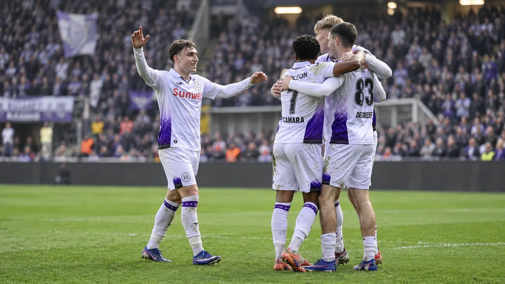 Een groep Anderlecht-spelers viert samen op het veld in wit-paars tenue.