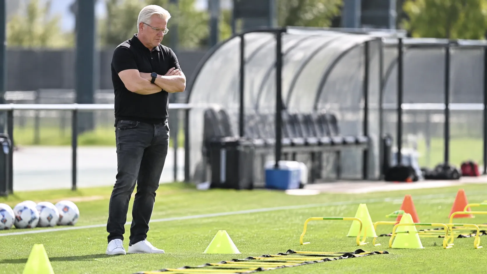 Lars Friis staat langs een trainingsveld en observeert de oefenmaterialen.