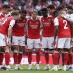 Een groep Arsenal-spelers in rood-witte tenues verzamelt zich op het veld voor een wedstrijd.