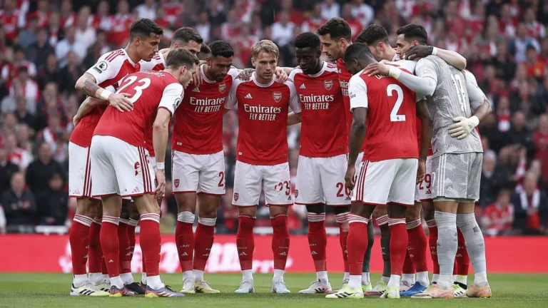 Een groep Arsenal-spelers in rood-witte tenues verzamelt zich op het veld voor een wedstrijd.
