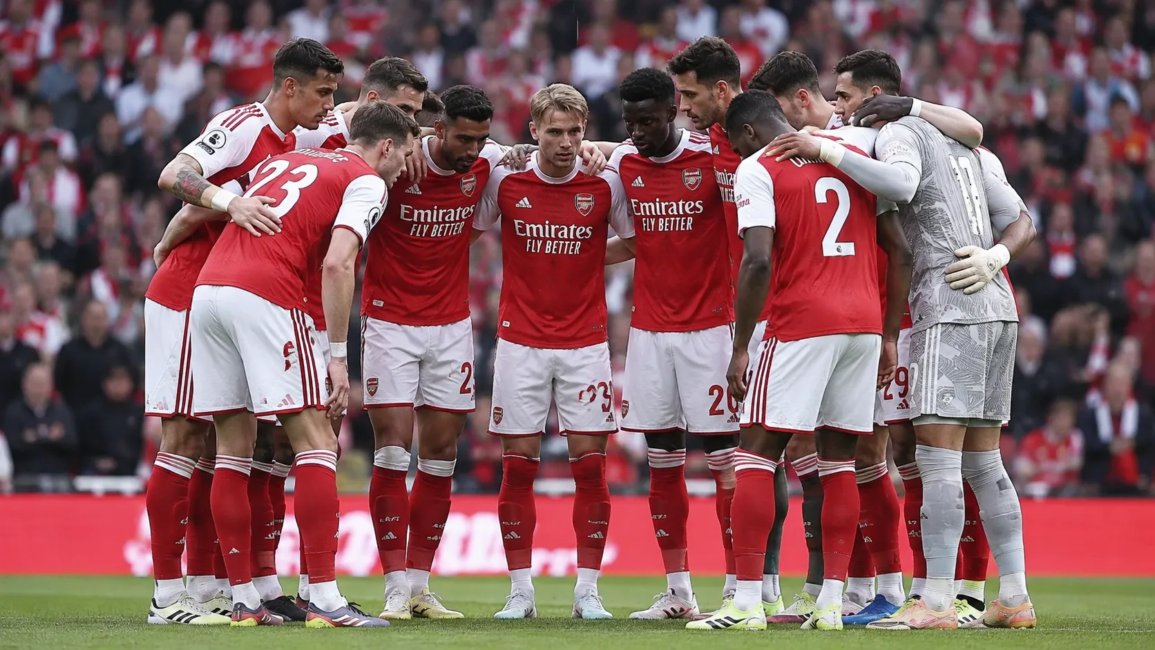 Een groep Arsenal-spelers in rood-witte tenues verzamelt zich op het veld voor een wedstrijd.