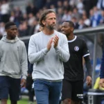 Een groep technische stafleden wandelt langs de zijlijn van een voetbalstadion.