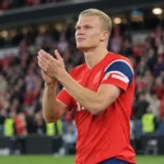 Erling Haaland in een rood Noors shirt terwijl hij na een WK-wedstrijd de supporters applaudisseert.