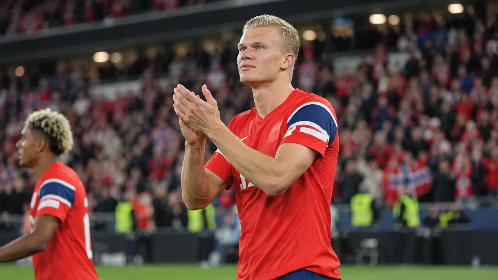 Erling Haaland in een rood Noors shirt terwijl hij na een WK-wedstrijd de supporters applaudisseert.
