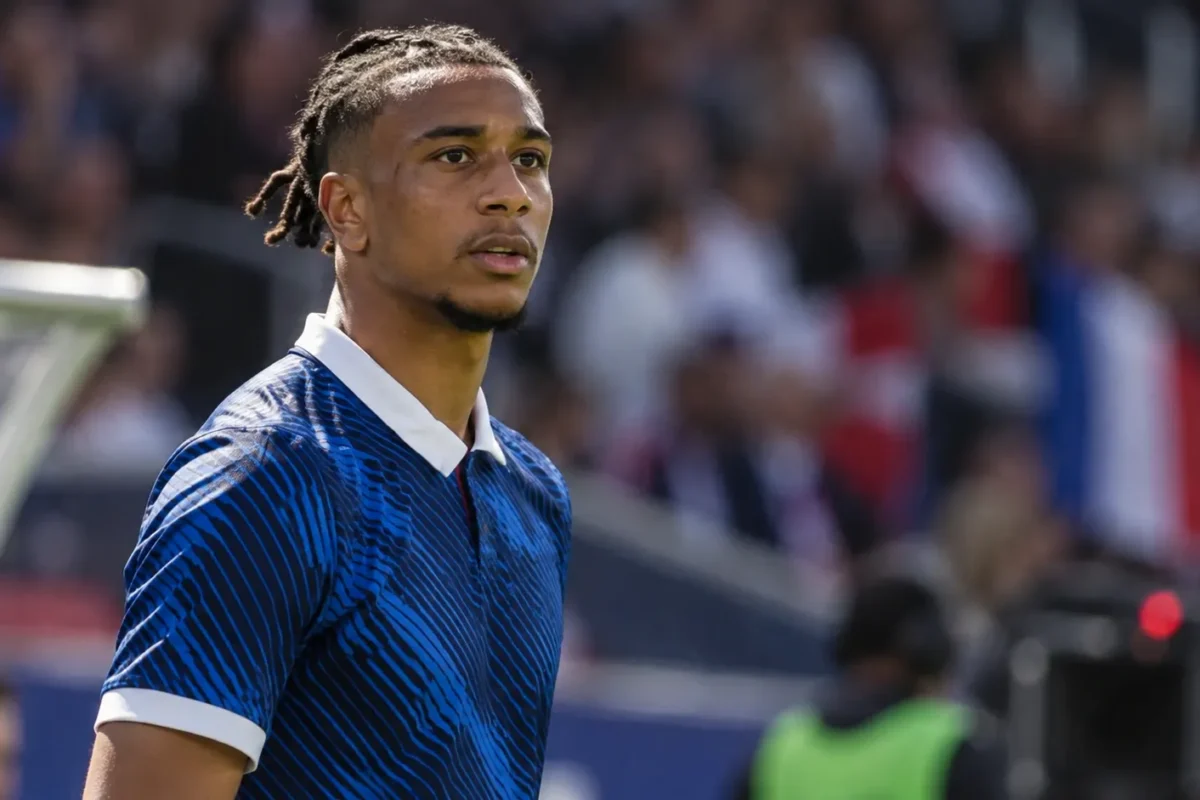 Michael Olise in een donkerblauw nationaal tenue aan de zijlijn van een voetbalstadion.