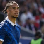 Michael Olise in een donkerblauw nationaal tenue aan de zijlijn van een voetbalstadion.