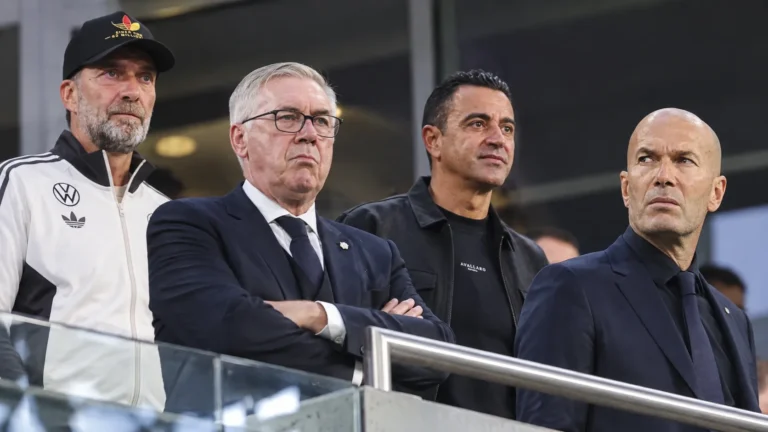 Vier bondscoaches in de overdekte tribunezone van een stadion.