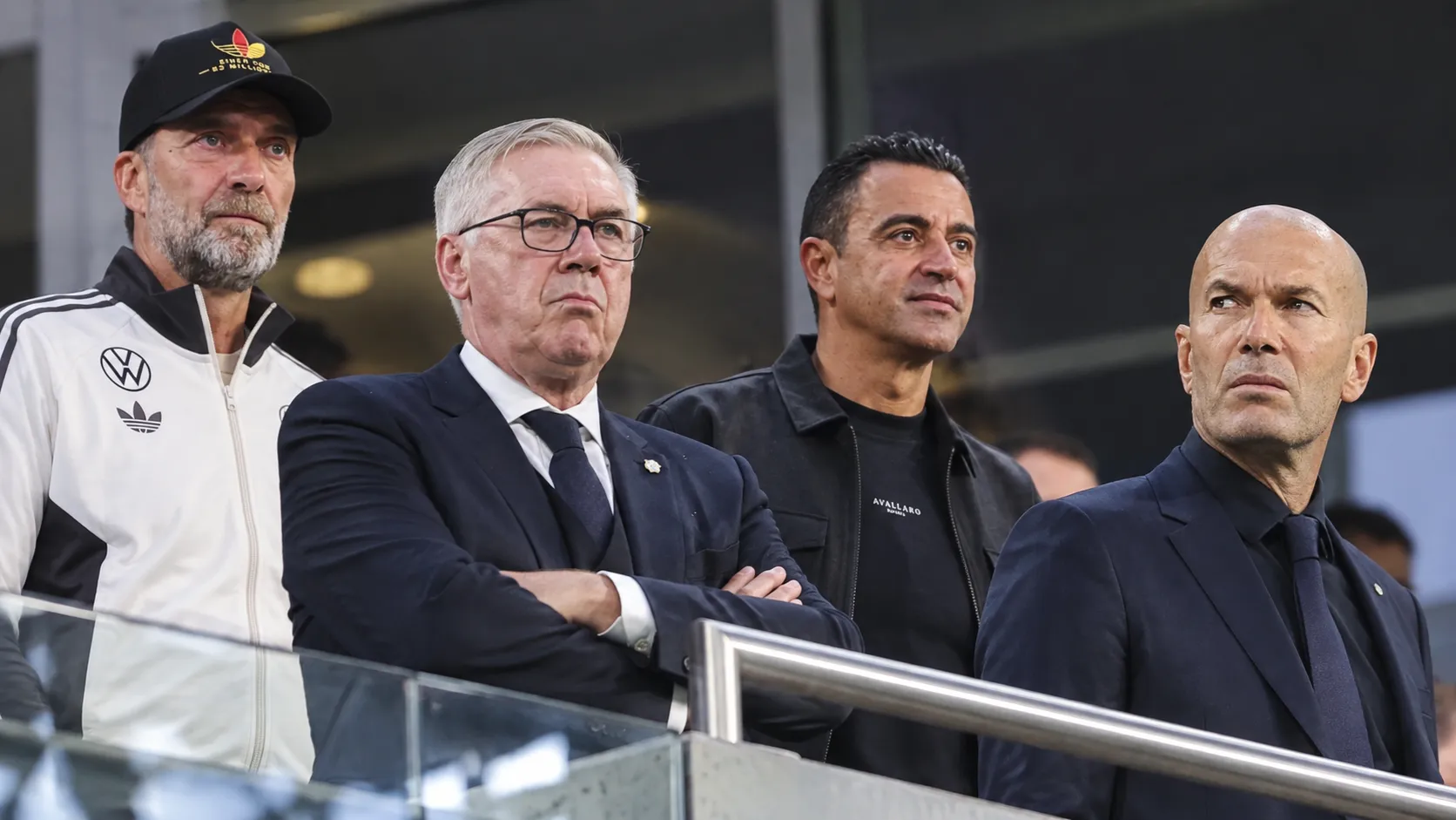 Vier bondscoaches in de overdekte tribunezone van een stadion.