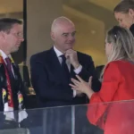 Meerdere voetbalofficials in formele kleding in een VIP-loge van een stadion.