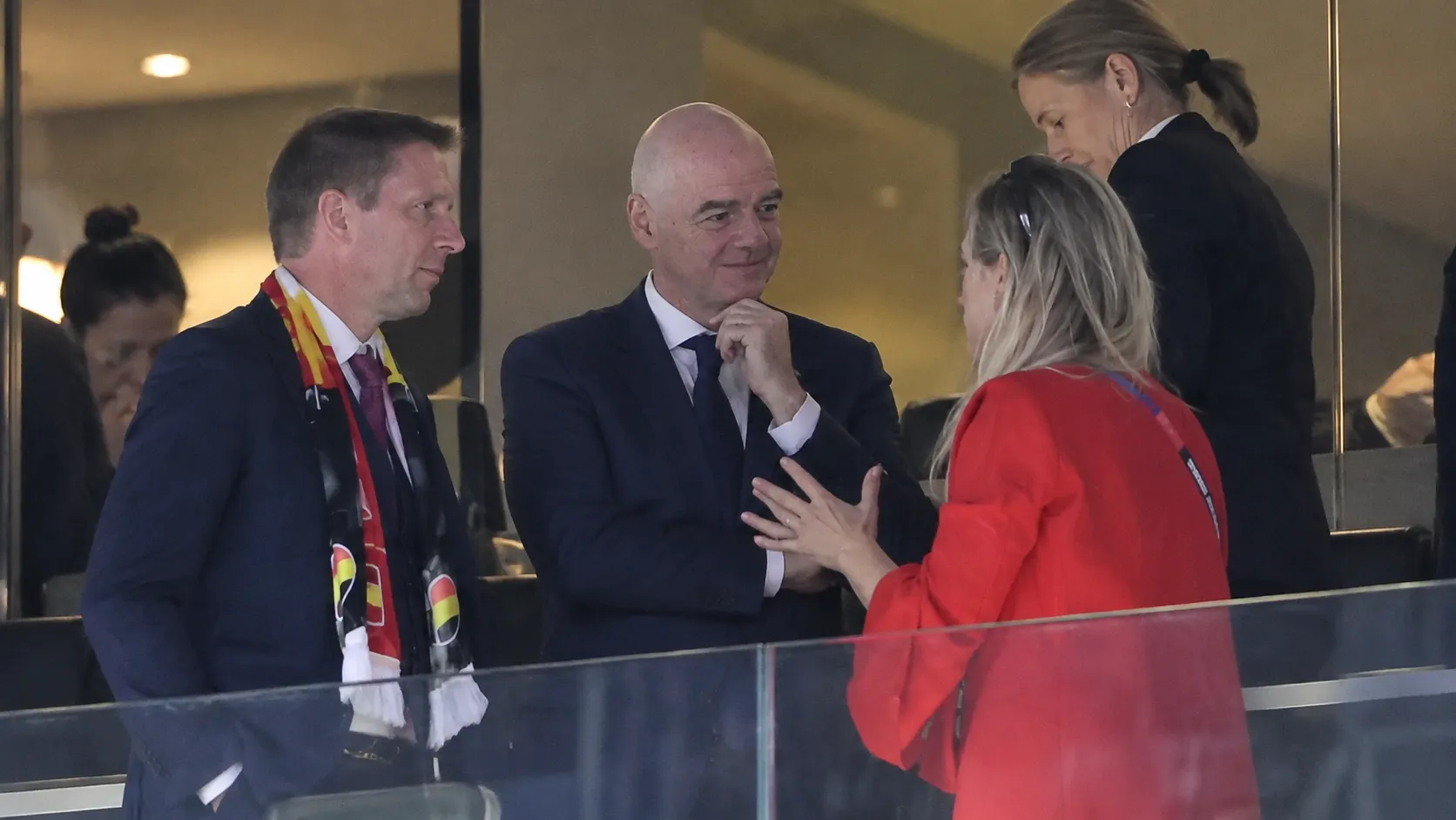 Meerdere voetbalofficials in formele kleding in een VIP-loge van een stadion.