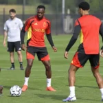 Een groep Belgische spelers in rood-zwarte trainingskleding tijdens een training op een grasveld.