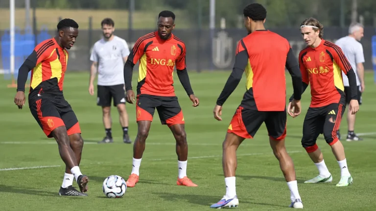 Een groep Belgische spelers in rood-zwarte trainingskleding tijdens een training op een grasveld.