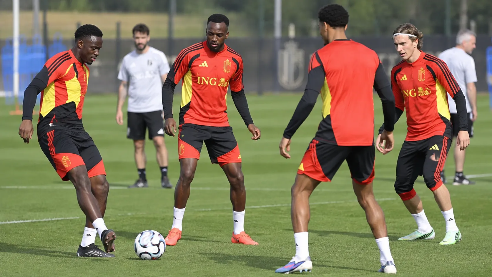 Een groep Belgische spelers in rood-zwarte trainingskleding tijdens een training op een grasveld.
