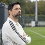 Een coach van Anderlecht staat naast het trainingsveld bij een vast clubembleem.