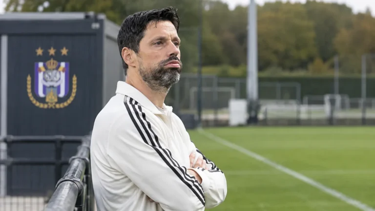 Een coach van Anderlecht staat naast het trainingsveld bij een vast clubembleem.