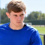 Max Dean in blauw sportshirt tijdens een gefocust moment in een buitenomgeving.