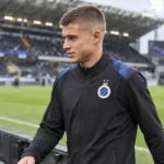 Nicolò Tresoldi in een zwarte trainingsjas van Club Brugge naast het veld.