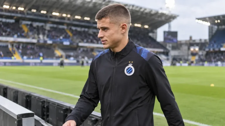 Nicolò Tresoldi in een zwarte trainingsjas van Club Brugge naast het veld.