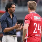 Een Antwerpse coach overlegt langs het veld met een speler in rood tenue.
