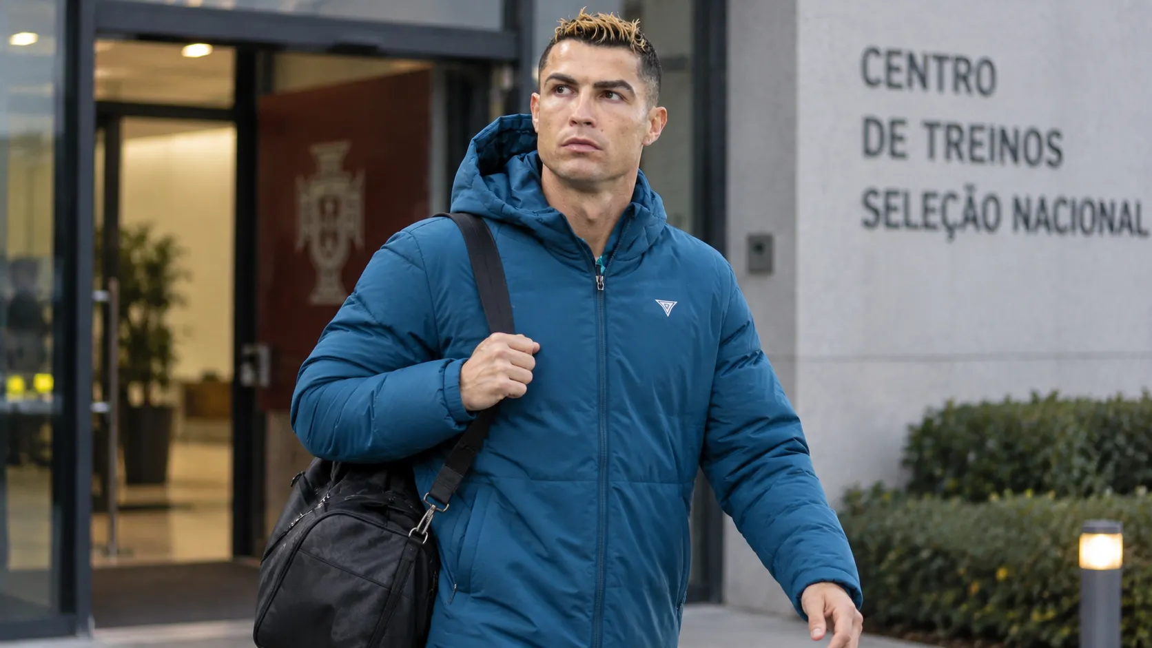 Cristiano Ronaldo in een blauwe gewatteerde jas bij het verlaten van een trainingscomplex.