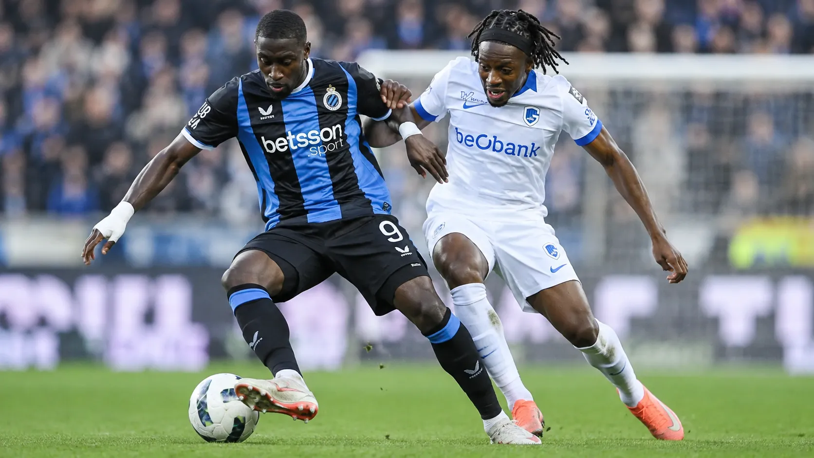 Twee voetballers van Club Brugge en KRC Genk vechten om balbezit in een duel.